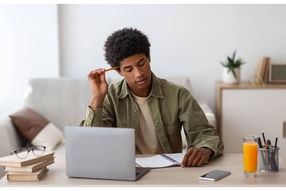 Thoughtful black teen guy passing hard exam or online test on laptop at home